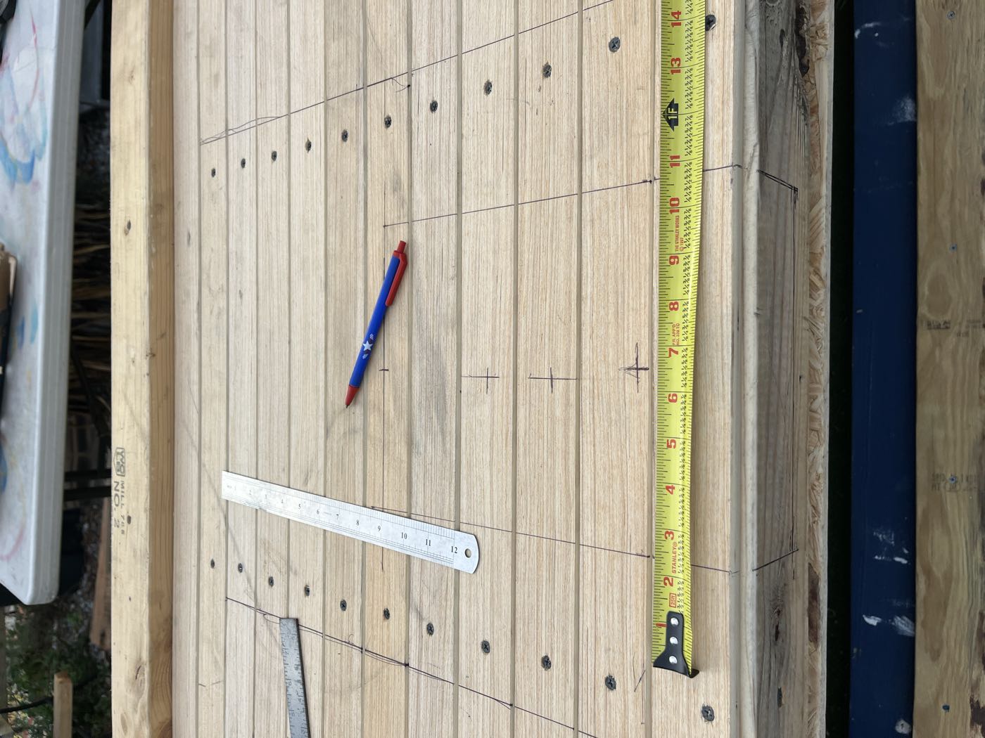 Tape measure and pencil marks laid across the sanded deck boards